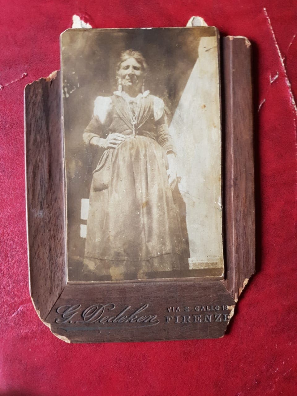 Sepia cabinet card of Grandma Corvelli standing in a long dress and apron, mounted on a dark card stamped G. Dedeken, Via S. Gallo, Firenze