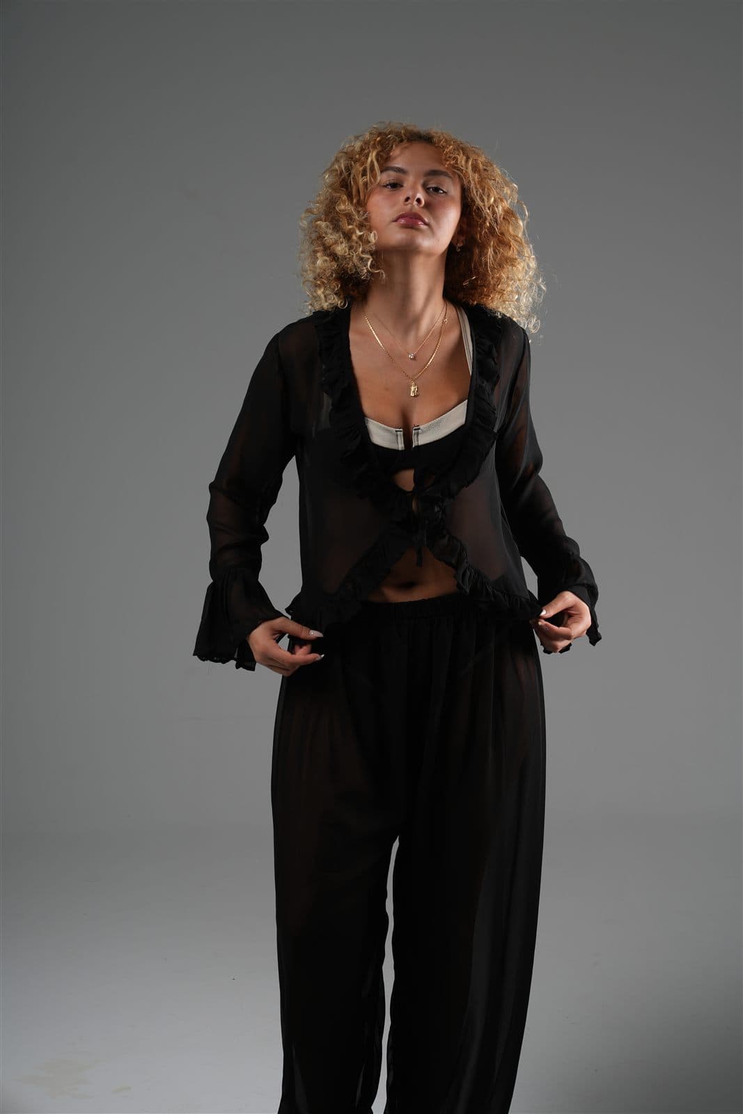 Model in a black sheer chiffon blouse with ruffled edges and bell cuffs